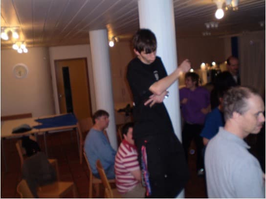 Ein junger Mann in Schwarz lehnt an einer weißen Säule inmitten einer Gruppe von Menschen.